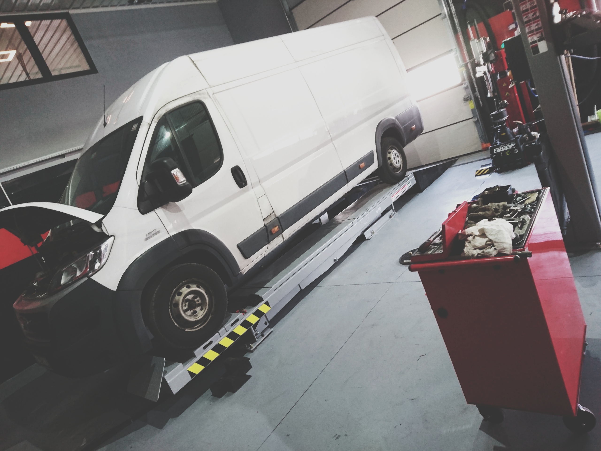 Biały dostawczy bus uniesiony na podnośniku nożycowym w warsztacie specjalizującym się w obsłudze pojazdów dostawczych